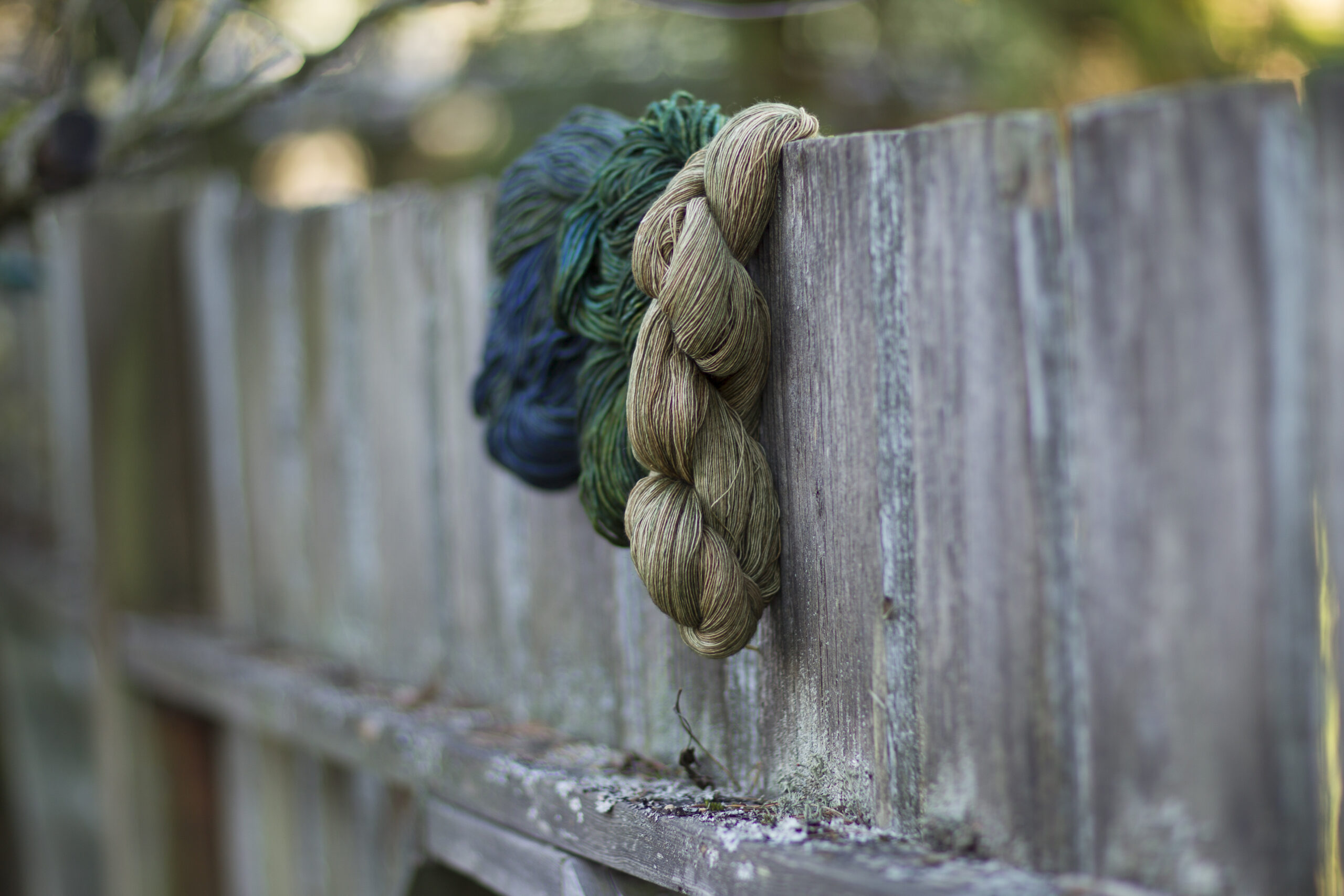 Two bundles of yarn hanging over a wooden fence.